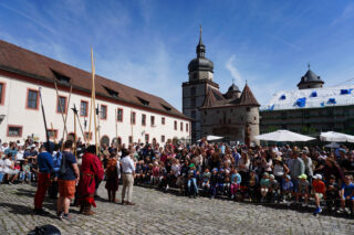 Zahlreiche Museumsfestbesucher bestaunen die Vorführung: Historisches Fechten. Die Festung Marienberg im Hintergrund erstrahlt im Sonnenschein.