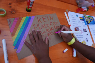 Ein Kind bastelt ein buntes Schild mit der Aufschrift: Kein Platz für Diskriminierung. Ein Kreativprogramm zur Ausstellung Franken fordert Freiheiten.