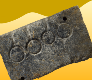 Eine abgenutzte Metallplakette mit vier eingravierten Kreisen und zwei Löchern, schräg vor einem gelb-orangefarbenen Hintergrund.