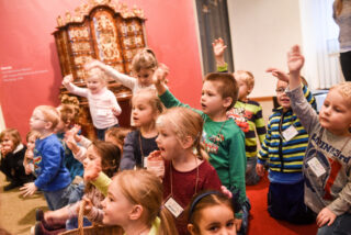 Eine Gruppe von kleinen Kindern macht begeistert bei einem Programm mit. Die Kinder lachen und viele melden sich.