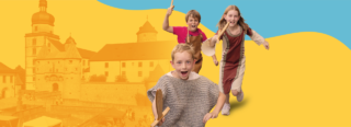 Drei Kinder laufen vor einer gelb-orangefarbenen Stadtansicht mit historischen Gebäuden, während das vornstehende Kind eine Holzschiene hält.