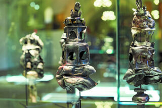 Ein Set von dekorativen, silbernen Objekten mit filigranen Details in einer Museumsausstellung, beleuchtet von sanftem Licht. Die Objekte zeigen verschiedene historische Designs und sind auf Glasregalen platziert.