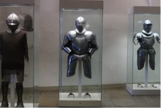 Drei Ritterrüstungen mit Helmen, Harnischen und Kettenhemden in Vitrinen eindrucksvoll beleuchtet.