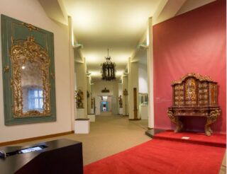 Ein Blick in den Ausstellungsraum "Barock" des Museums für Franken. Dort ist ein großer verzierter Spiegel und ein schöner Schreib-Schrank mit vielen geschnitzten Details zu sehen.