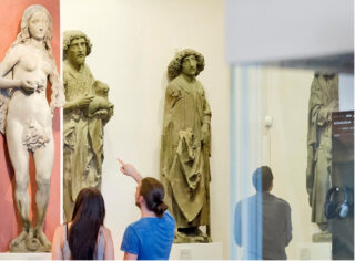 Besucher betrachten die Riemenschneiders Skulpturen im Riemenschneider-Saal. Sie zeigen auf eine Detail an seiner berühmten Figur "Eva".