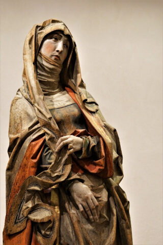 Eine Skulptur aus Holz von der nur der Kopf und die Schultern abgebildet sind. Sie zeigt die trauernde Maria. Sie ist bunt und sehr detailreich.