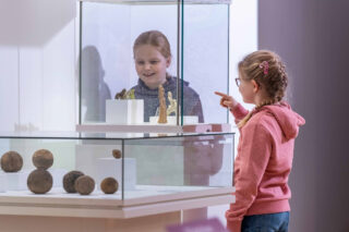 Zwei Mädchen stehen vor einer Vitrine.