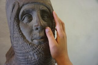 Eine Hand berührt eine Steinskulptur. Diese zeigt den Kopf eines Ritters. Bei Führungen für Blinde und Menschen mit Sehbeeinträchtigung dürfen echte Ausstellungsstücke berührt werden.