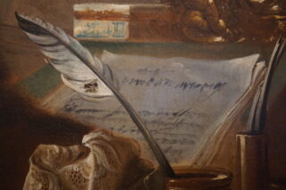 Ein Federkiel liegt auf einem handgeschriebenen Dokument, umgeben von einer Schreibtischunterlage und einem Glas Tinte. Im Hintergrund sind Notizkarten und weiteres Schreibzubehör sichtbar.