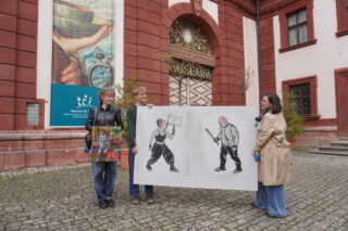 Jonna Fischer mit ihrem Bild "(Sch)merz", Lorenz Greshake mit seinem Bild „Kein Raum für Worte“ und Veronika Genslein, stellvertretende Direktorin des Museums für Franken, vor dem Museumseingang.